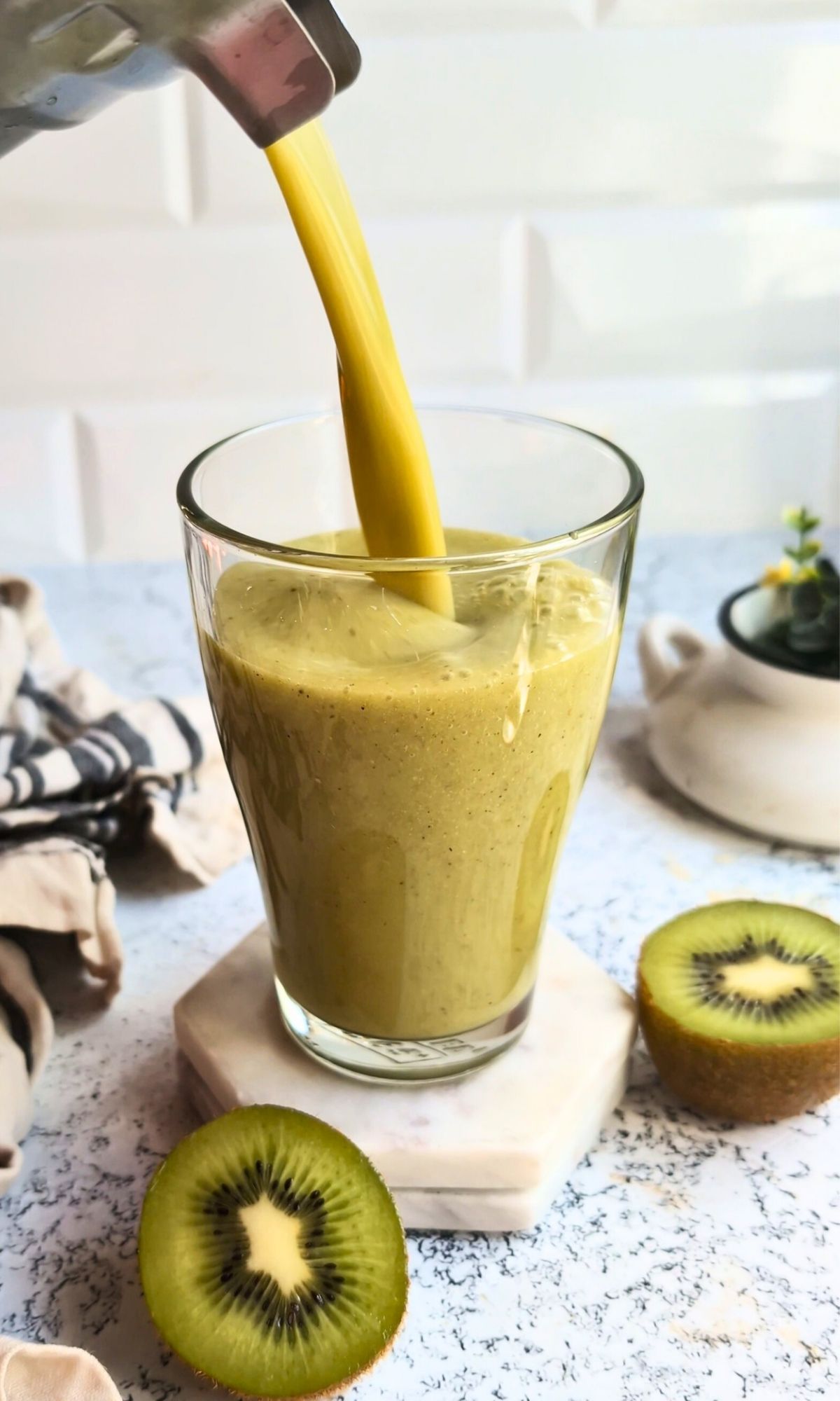 a blender pouring a green kiwi smoothie into a glass for a tasty and delicious tropical kiwi smoothie.