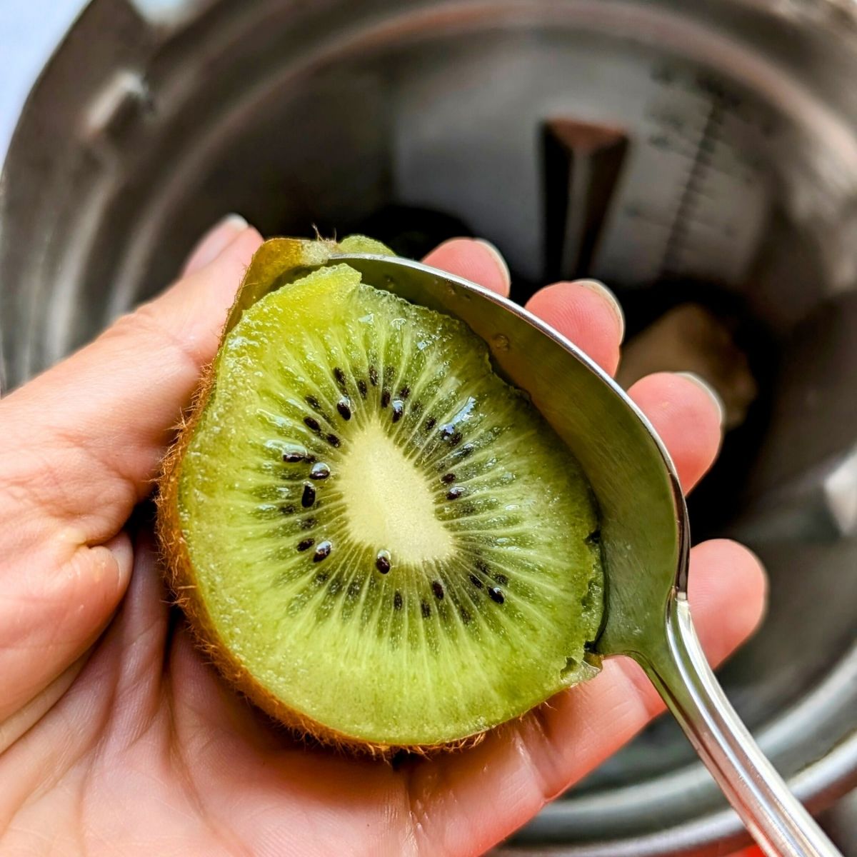 a hand scooping out the kiwi flesh with a spoon to make a smoothie.