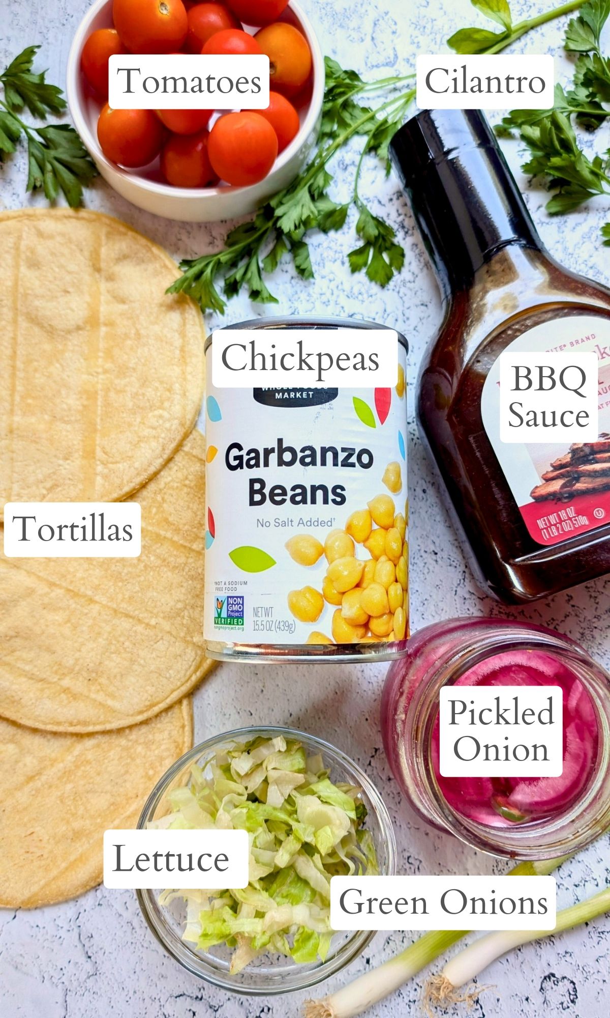 ingredients for bbq chickpea tacos like bbe sauce, pickled onions, cilantro, green onions, tomatoes, and tortillas.