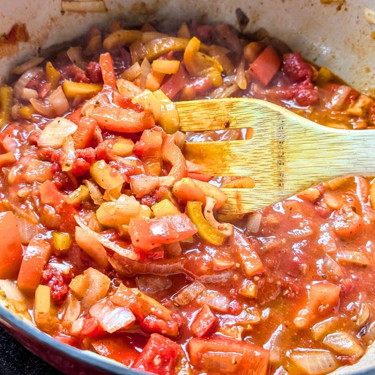 a pot with bell peppers, diced tomatoes, and tomato paste being simmered for a plant based cajun pasta sauce.