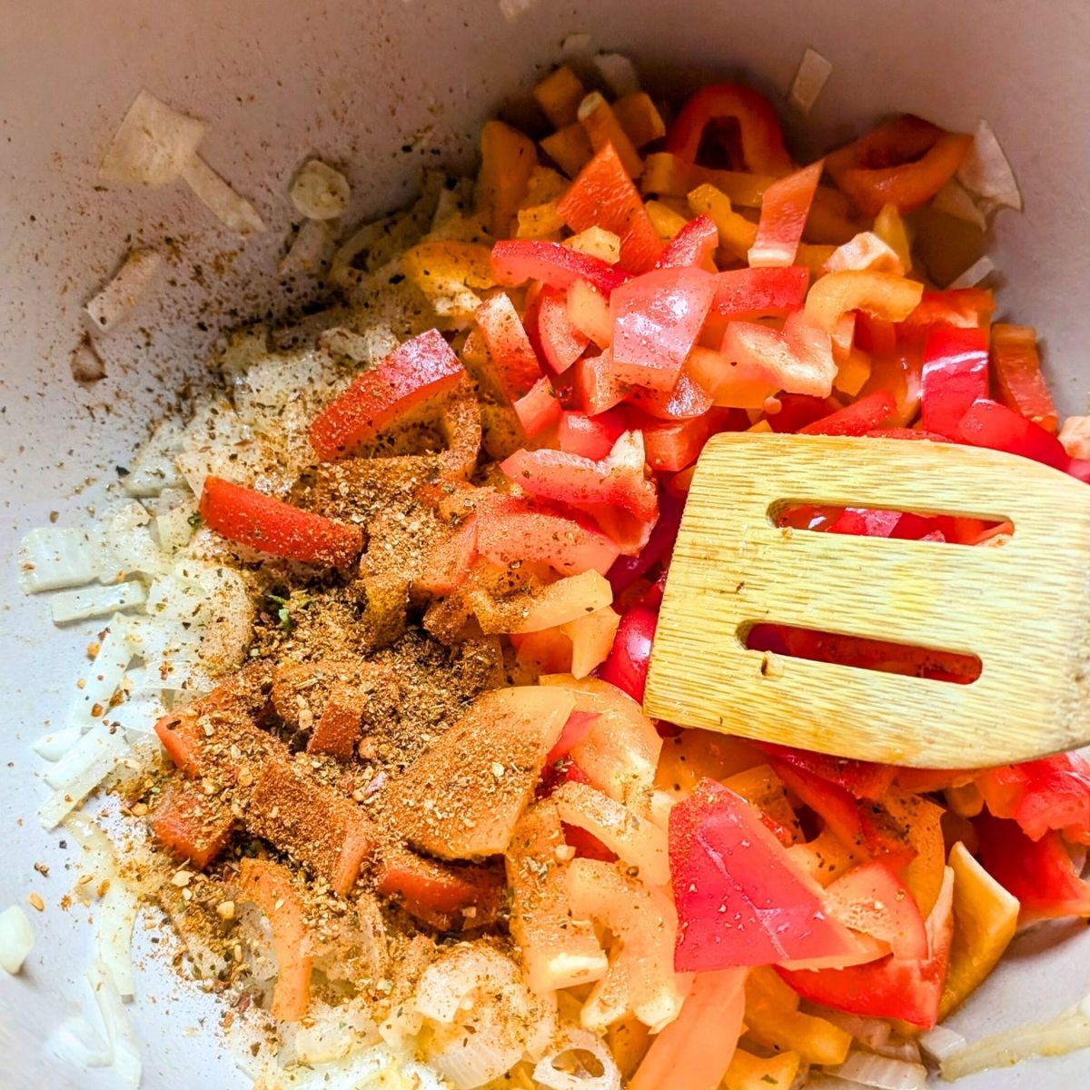 a pot with vegetarian creole pasta ingredients like onions, jalapeno peppers, and bell peppers being sauteed until brown.