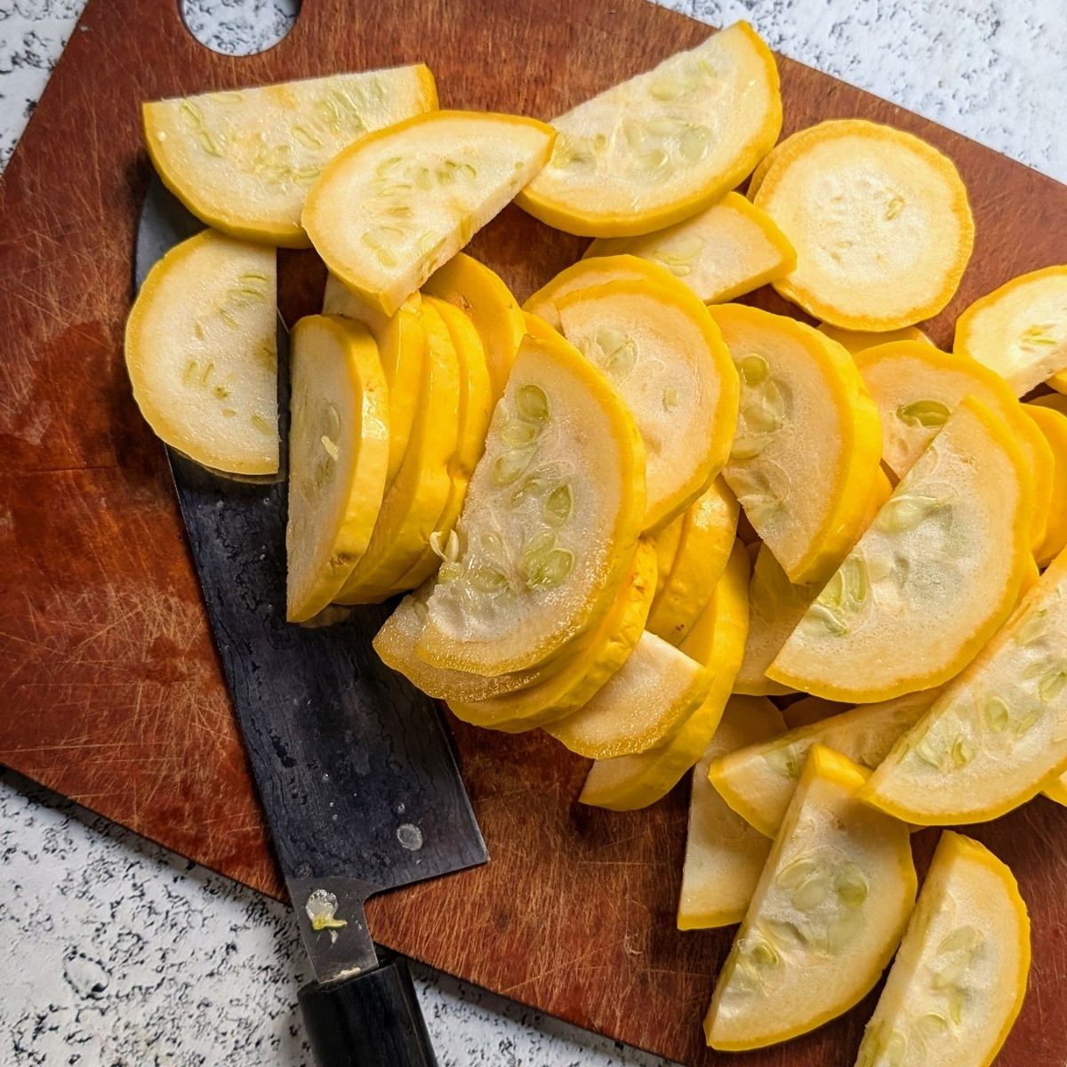 a knife slicing crookneck squash into pieces.