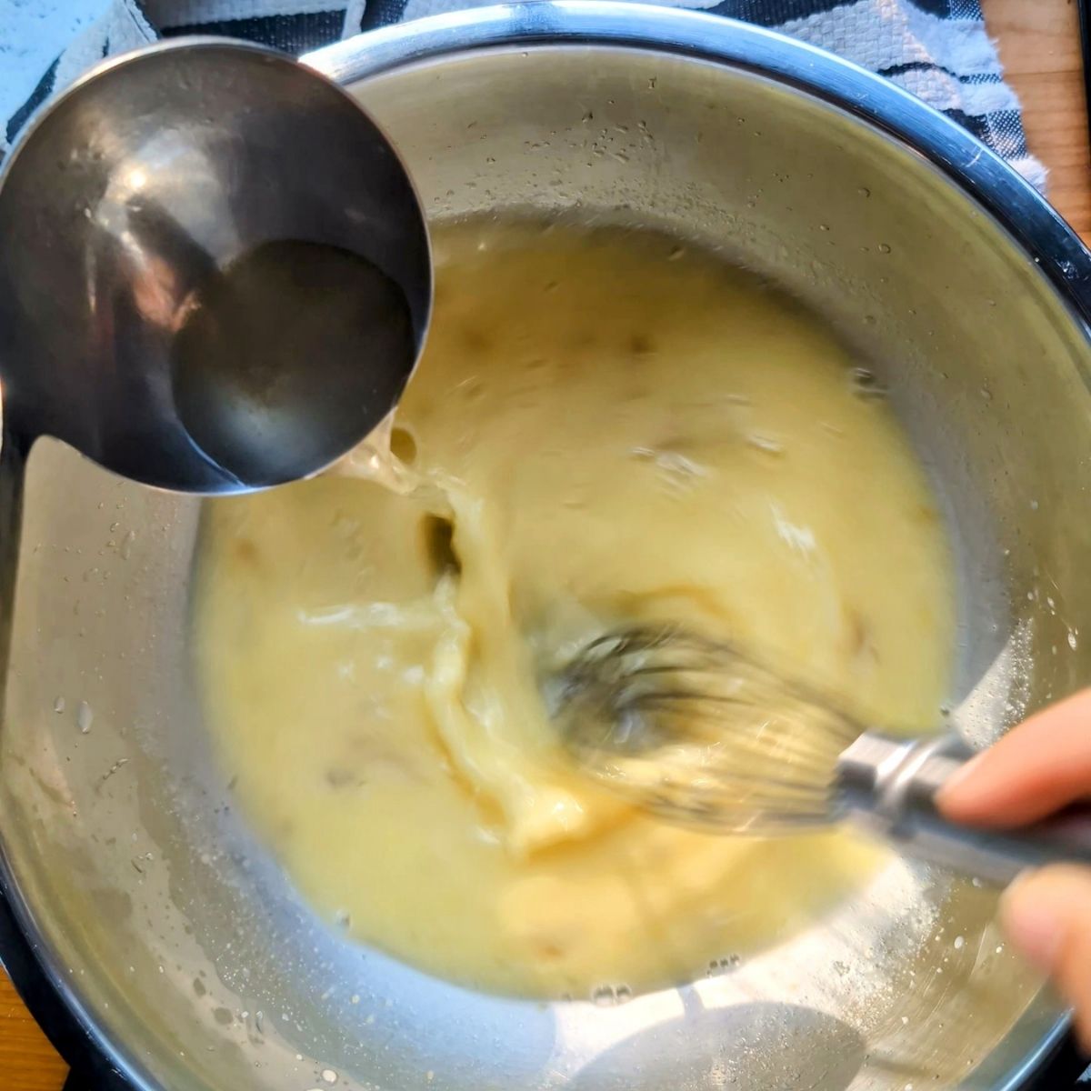 hot chicken soup being tempered and whisked into avgolemono broth for a orzo lemon chicken soup.