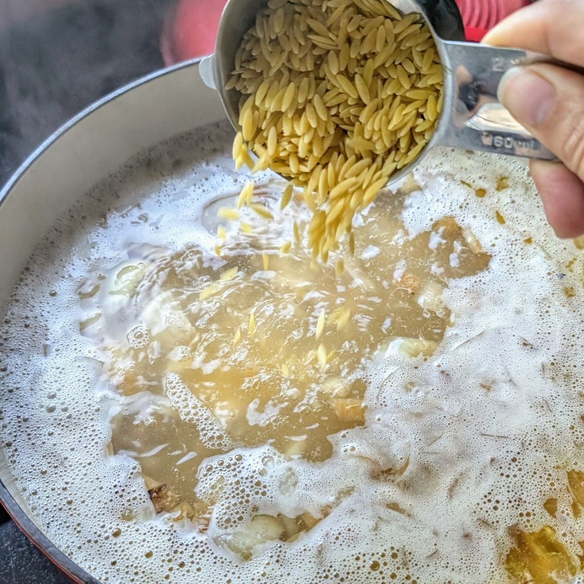 orzo soup being added to a pot for greek lemon chicken avgolemono soup with orzo.