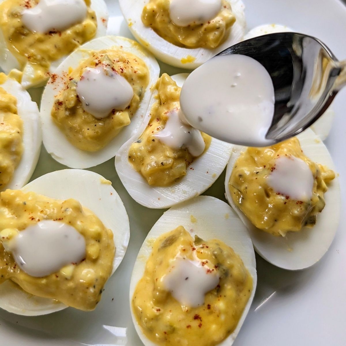 ranch dressing being drizzled on top of each deviled egg for extra flavor.