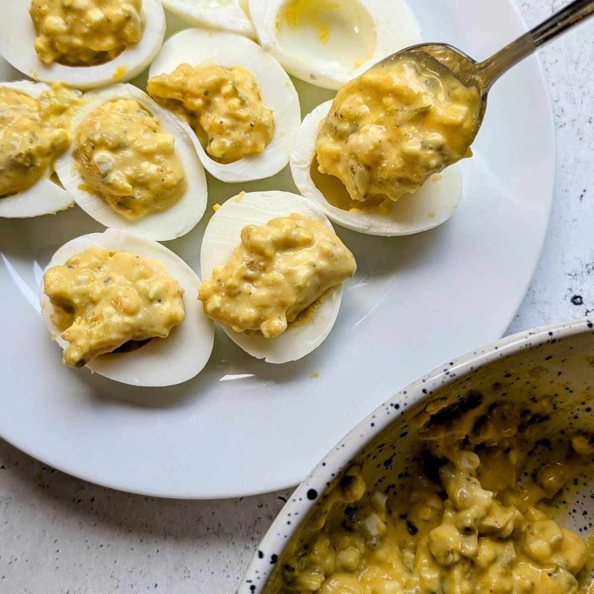 egg whites being filled with deviled egg filling with a spoon.