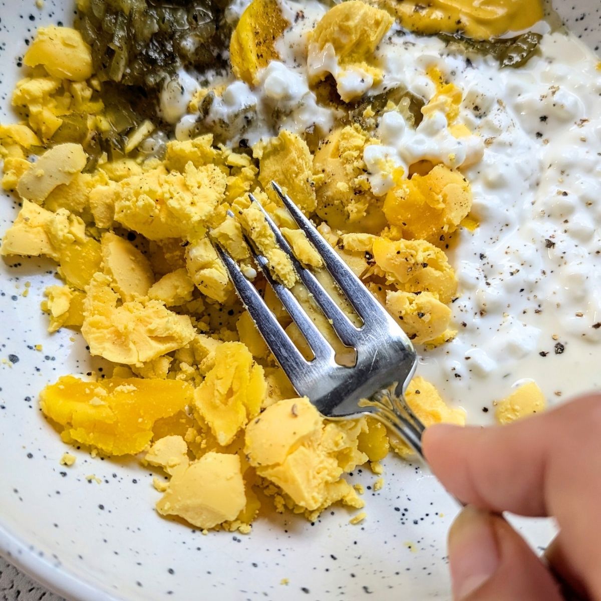 a fork mashing egg yolks for deviled eggs with cottage cheese filling and no mayo.