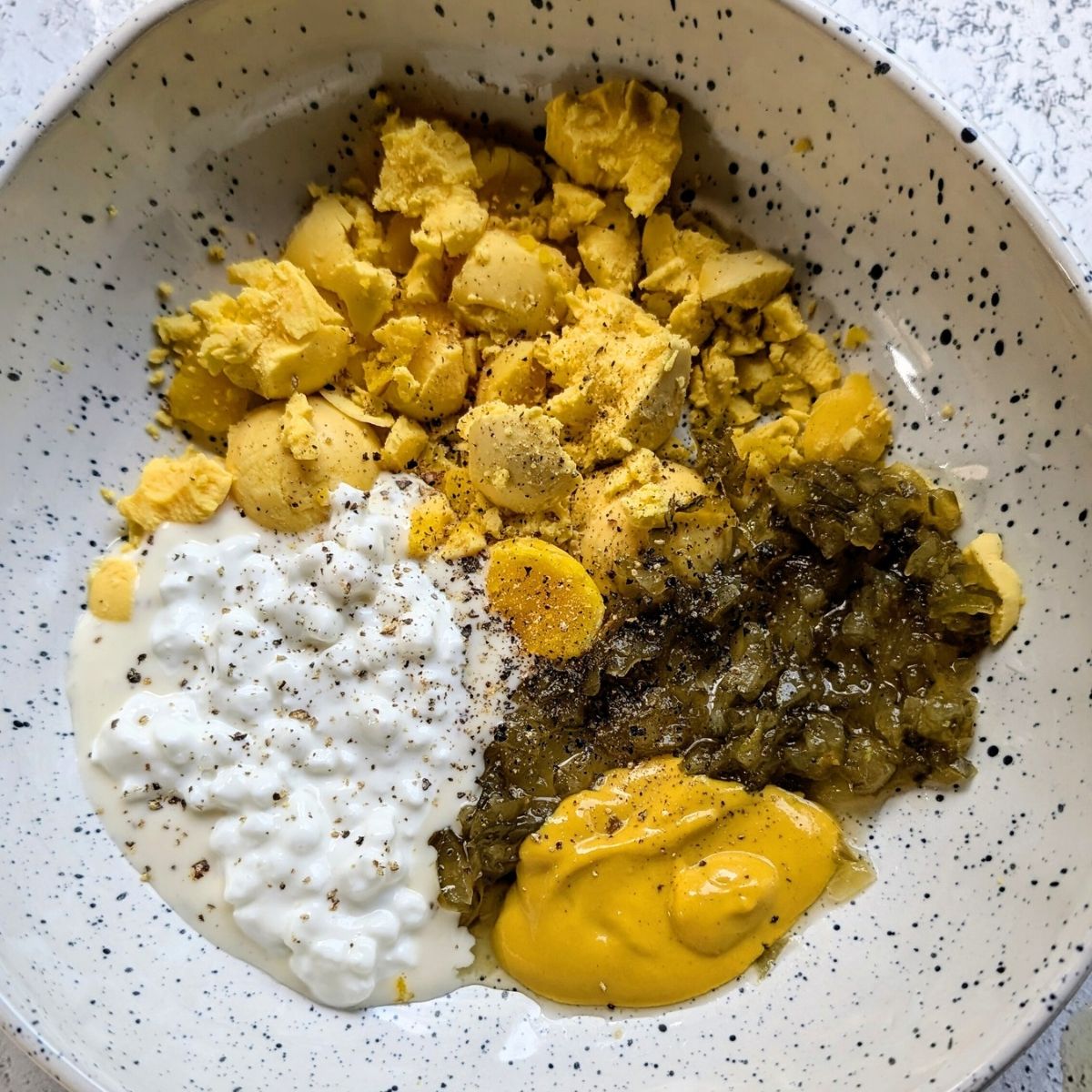 a mixing bowl filled with egg yolks, cottage cheese, sweet relish, mustard about to be mixed for deviled eggs.