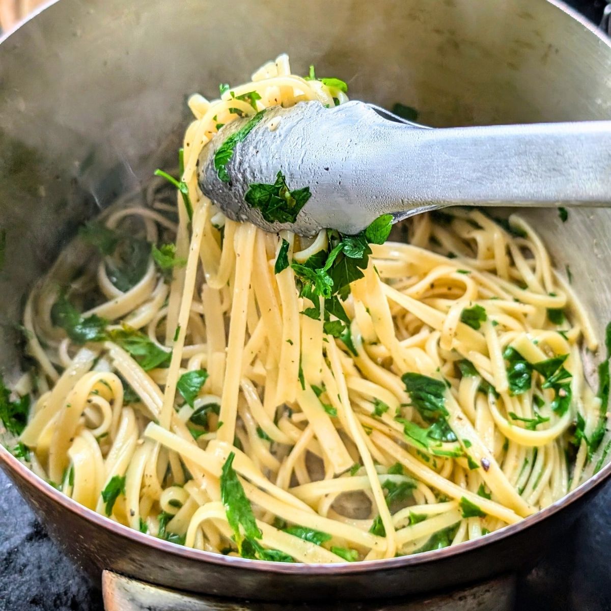 cooked pasta being tossed with fresh spinach that is wilted from the hot noodles with a pair of tongs.