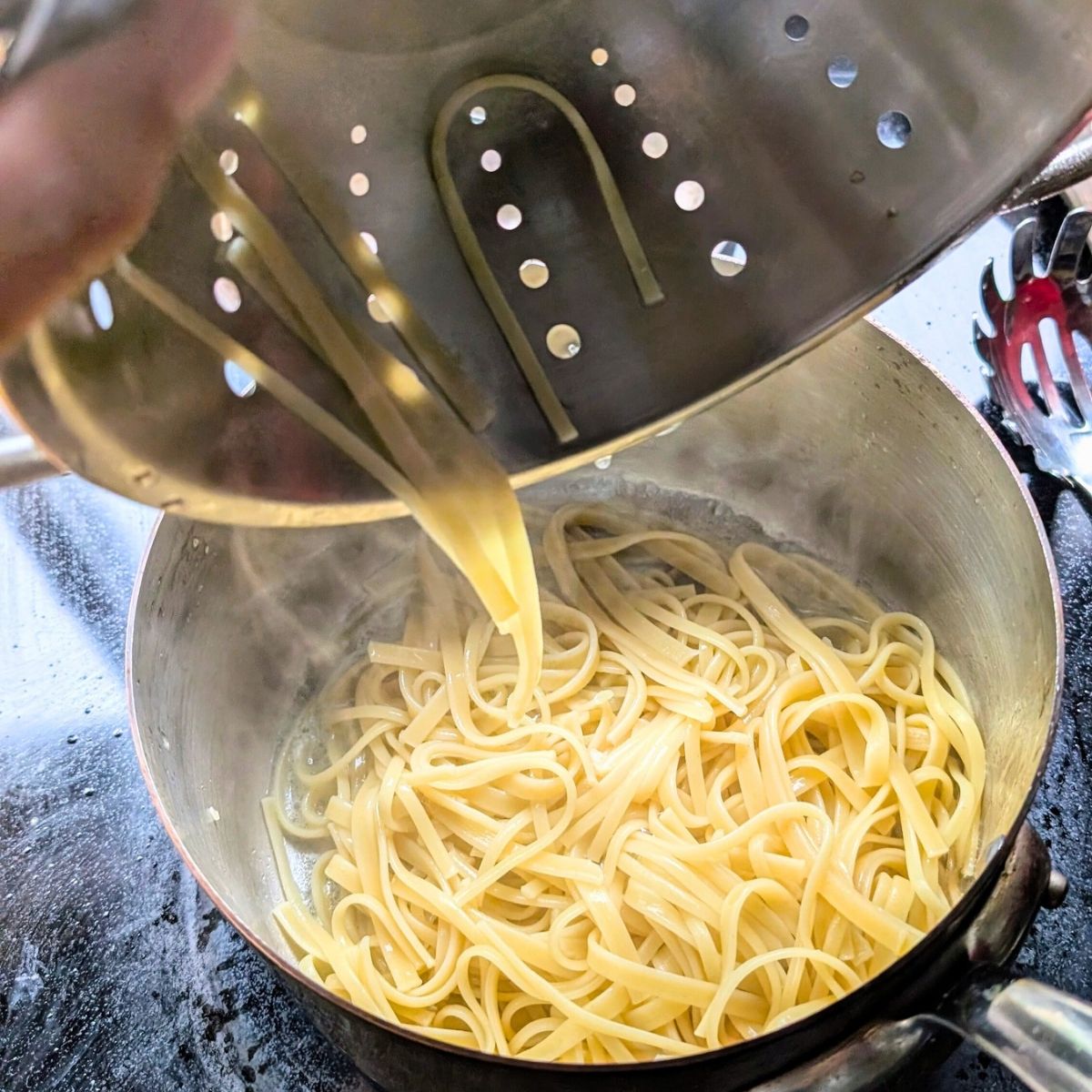 cooked noodles being added to a pot with a garlic and butter sauce.