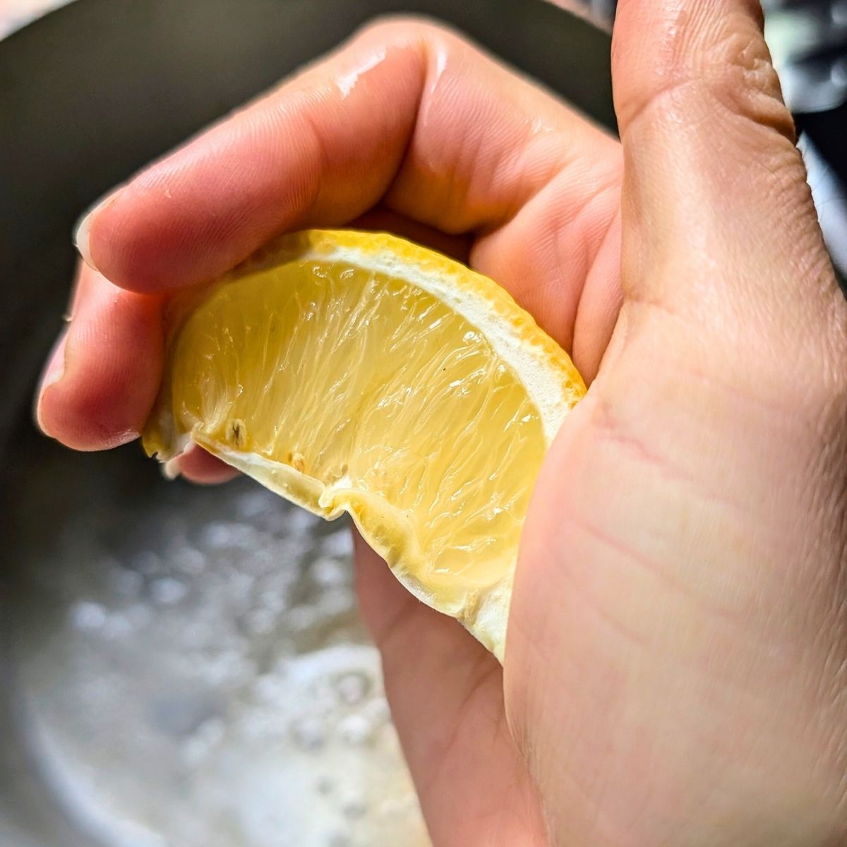 a hand squeezing fresh lemon juice into a pot with melted butter and sauteed garlic to make parsley pasta.