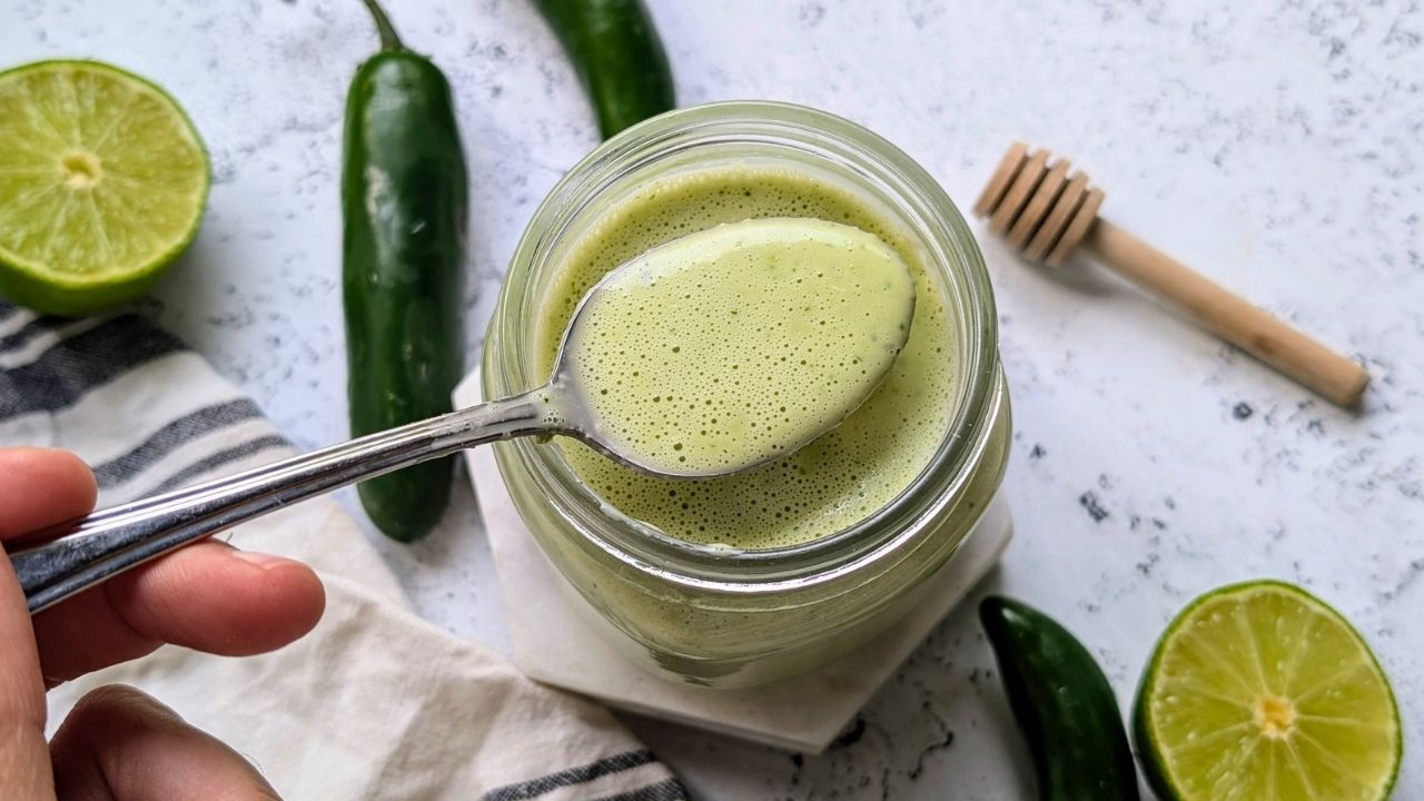 green dressing with serrano peppers, honey, and lime being scooped by a spoon to be drizzled over a salad.