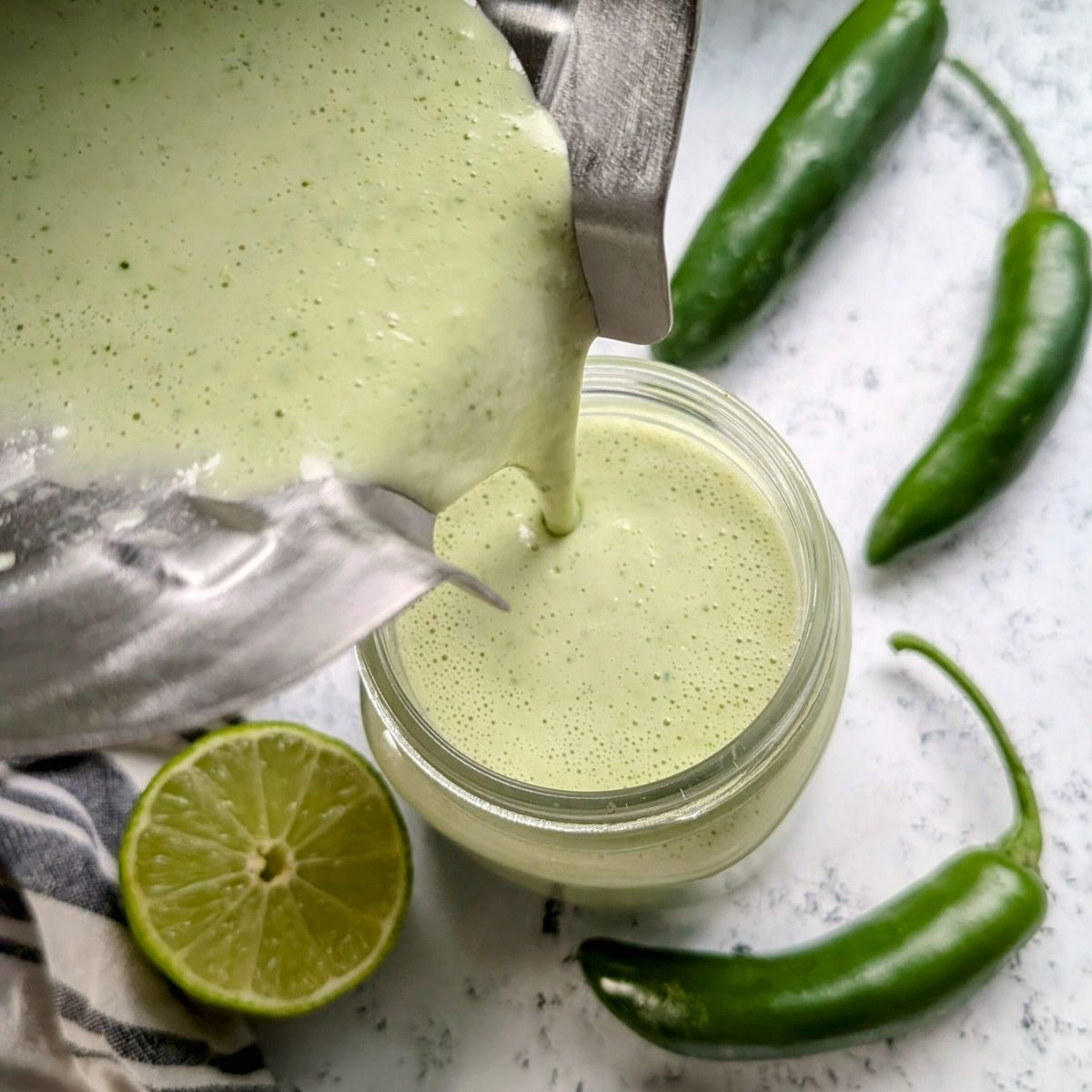 a blender pouring spicy serrano pepper dressing into a mason jar to dress a salad.