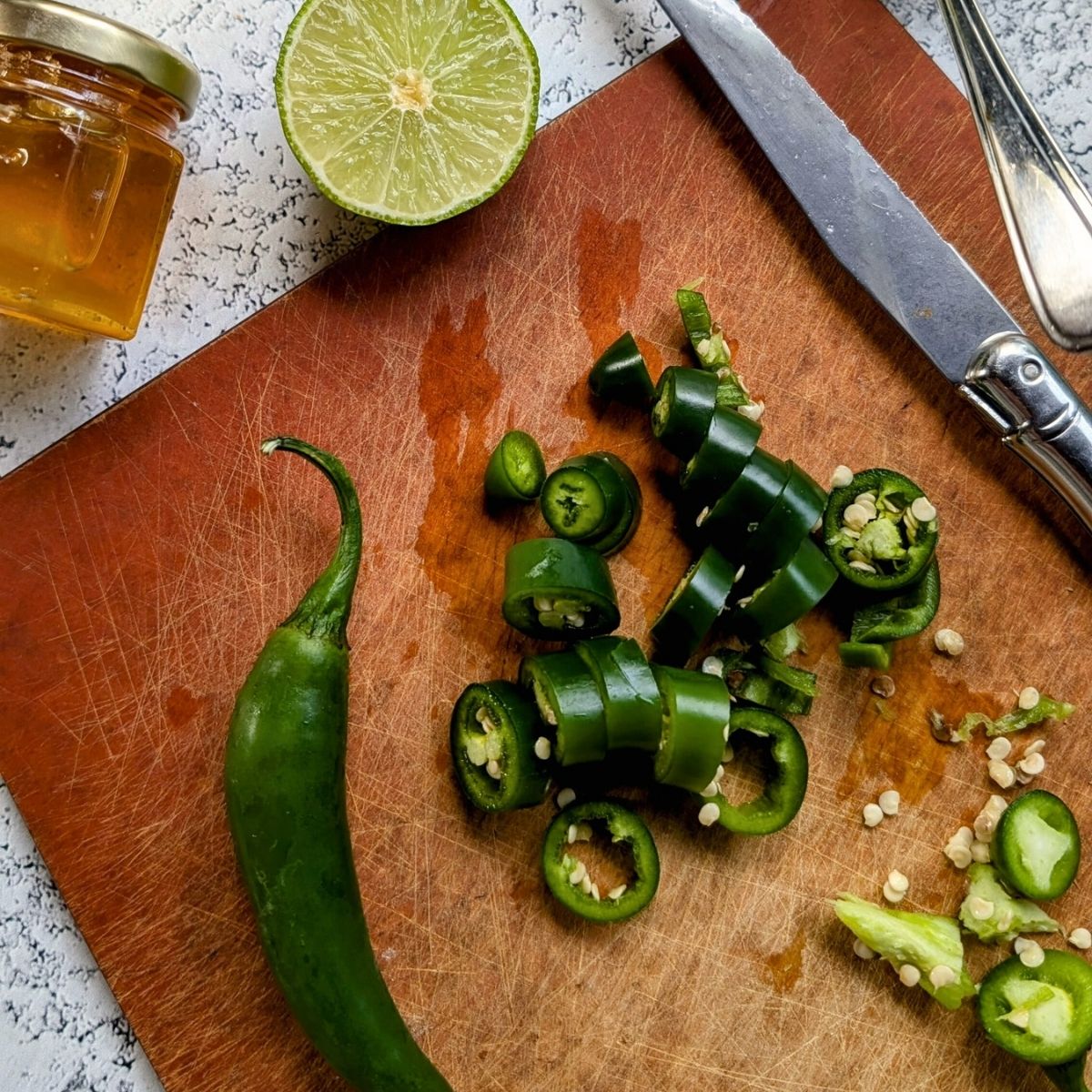 a cutting board with chopped serrano peppers, some with the ribs and seeds removed.