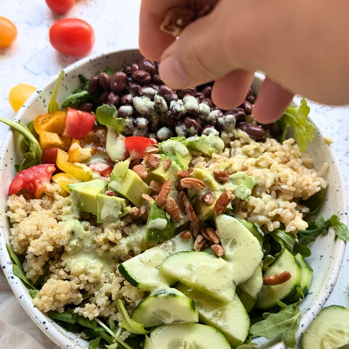 a hand adding chopped pecans to the top of a Southwest grain bowl salad like the alamo bowl.