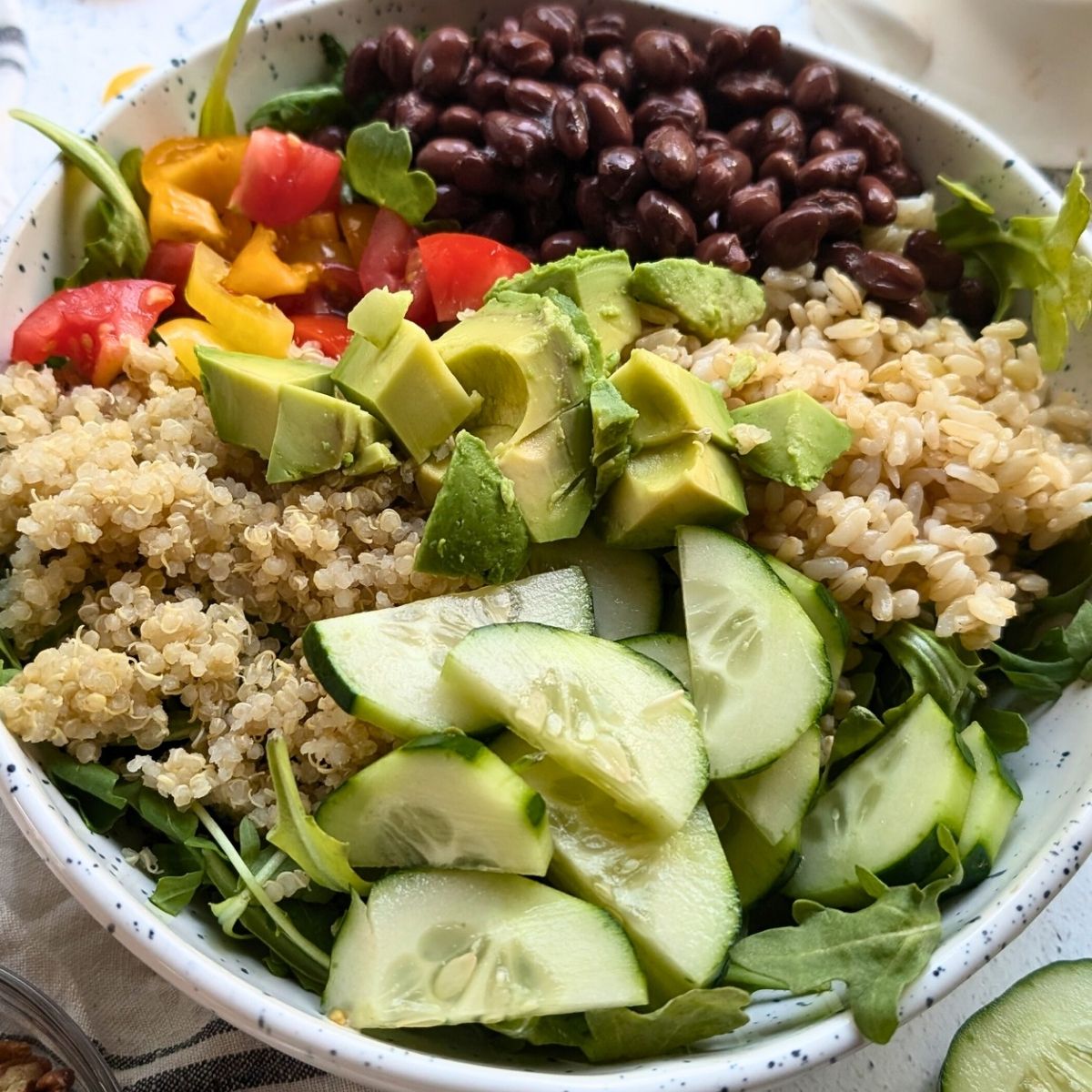 a large bowl filled with quinoa, black beans, cucumbers, tomatoes, and brown rice.