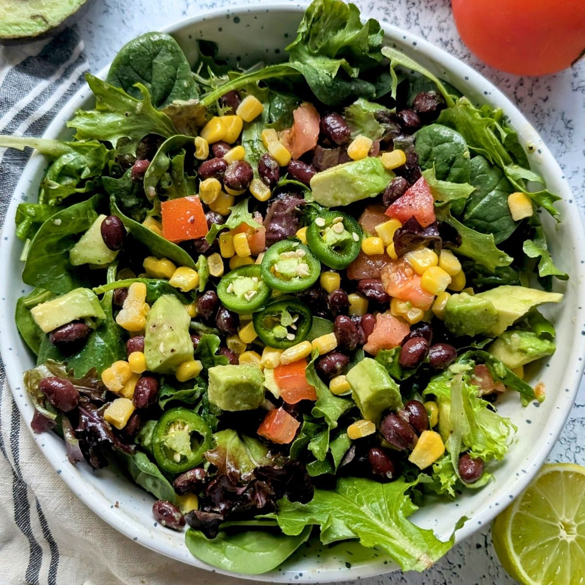 a big hearty southwest salad with corn, avocado, and black beans in a large bowl with mixed greens and jalapenos.