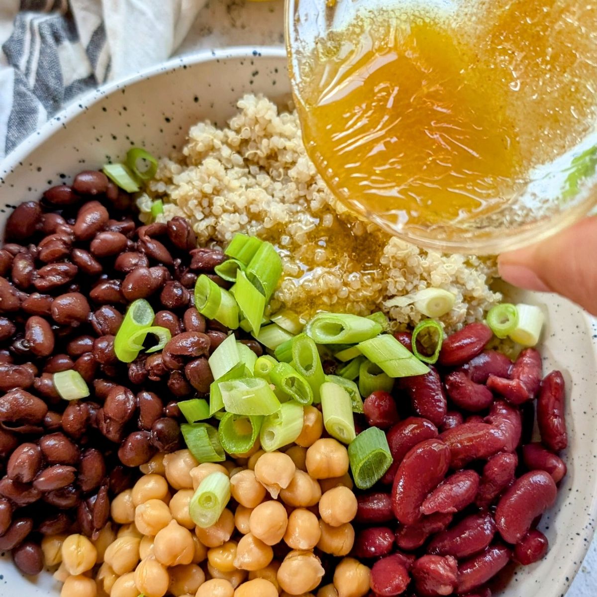 a hand pouring mixed vinaigrette over a bean salad with quinoa.