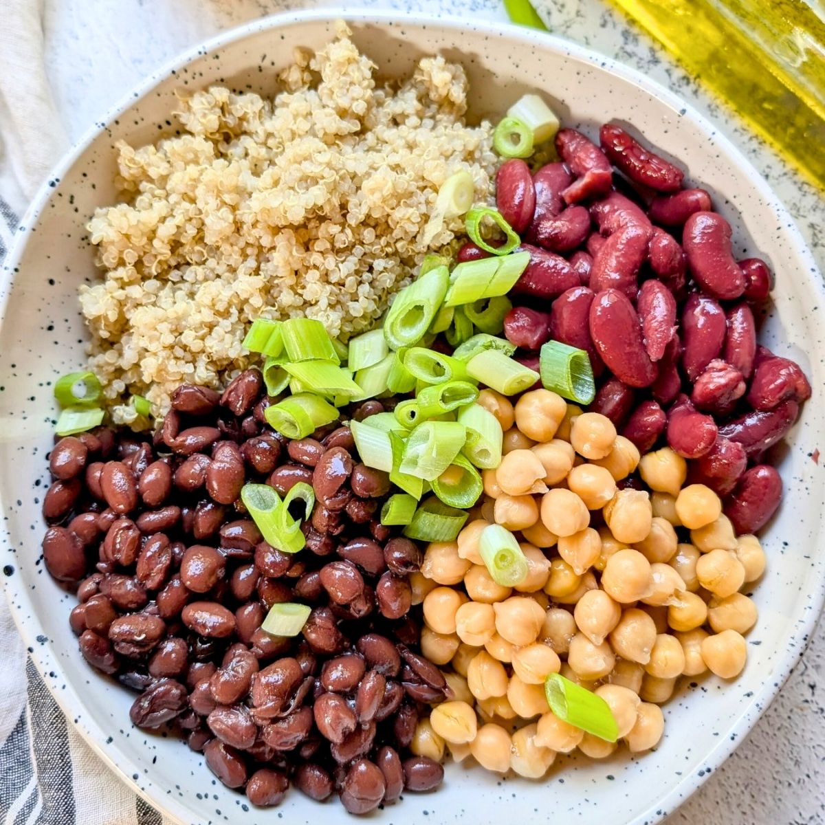 a large bowl with white quinoa, black beans, kidney beans, chickpeas, and green onions to make a tasty quinoa salad.