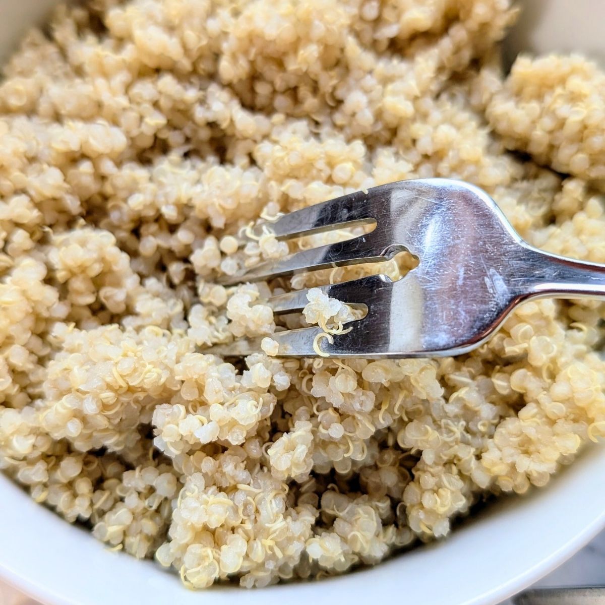 cooked white quinoa in a bowl being fluffed with a fork to make quinoa salad.