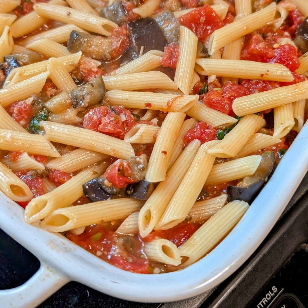 a baking dish with pasta, tomatoes, eggplant, and basil easy tasty vegetarian sicilian pasta sauce.