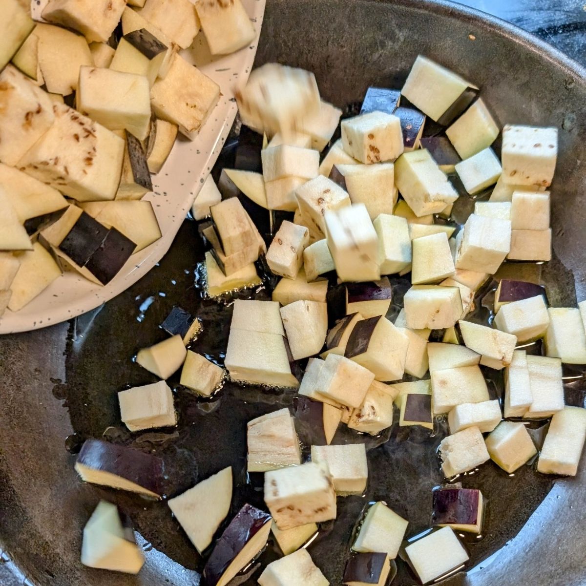 a skillet with olive oil garlic and fresh eggplant for sicilian pasta alla norma al forno recipe.