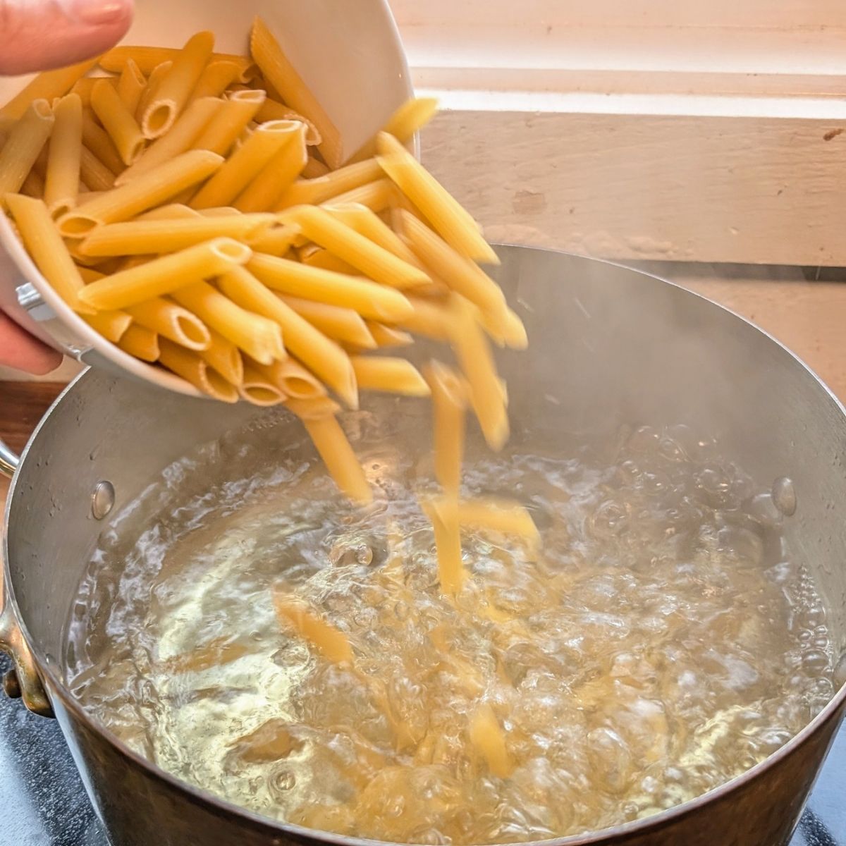 uncooked penne pasta being added to a pot of salted boiling water for pasta salad.