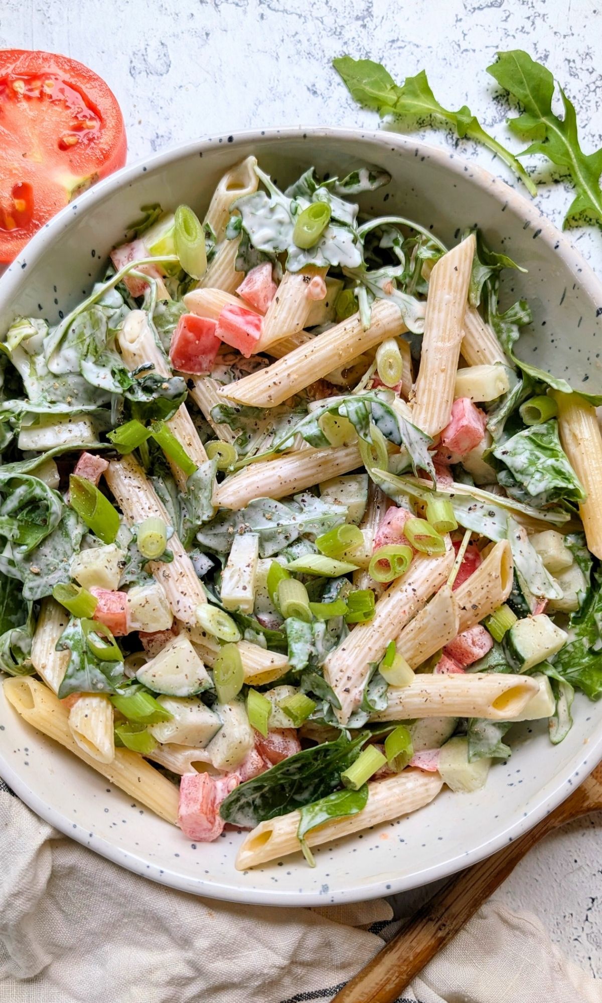 creamy penne pasta salad with arugula in a bowl topped with green onions.