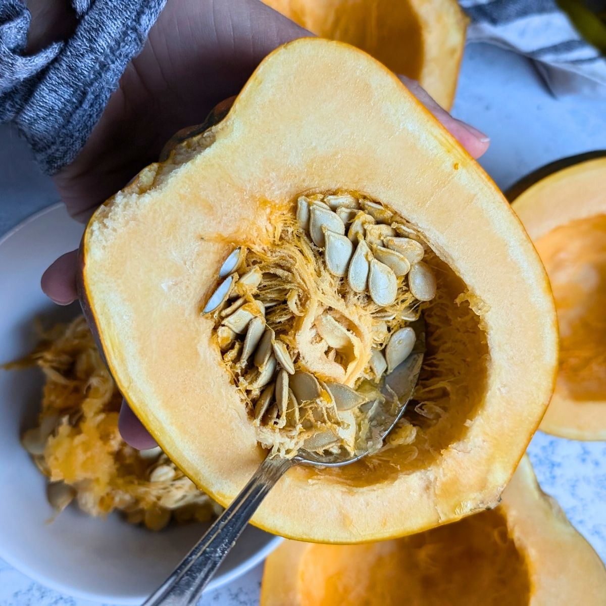 halved acorn squash with a spoon scooping out the seeds to make pasta sauce that's vegan and dairy free.