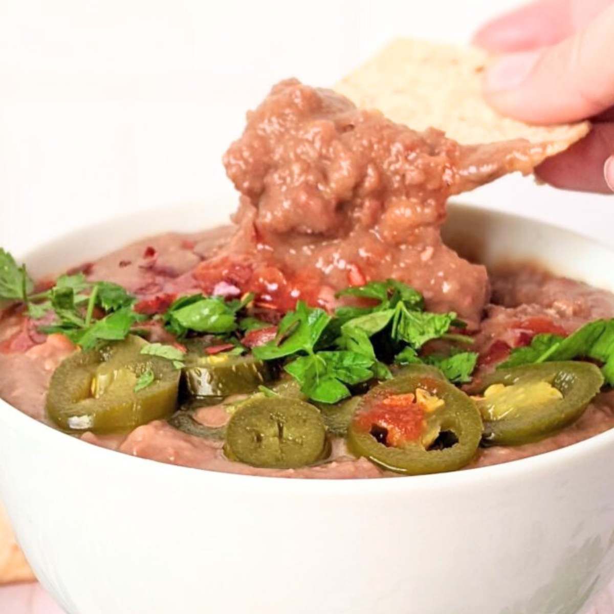 a hand dipping a tortilla chip into vegan instant pot refried beans with herbs and spices.