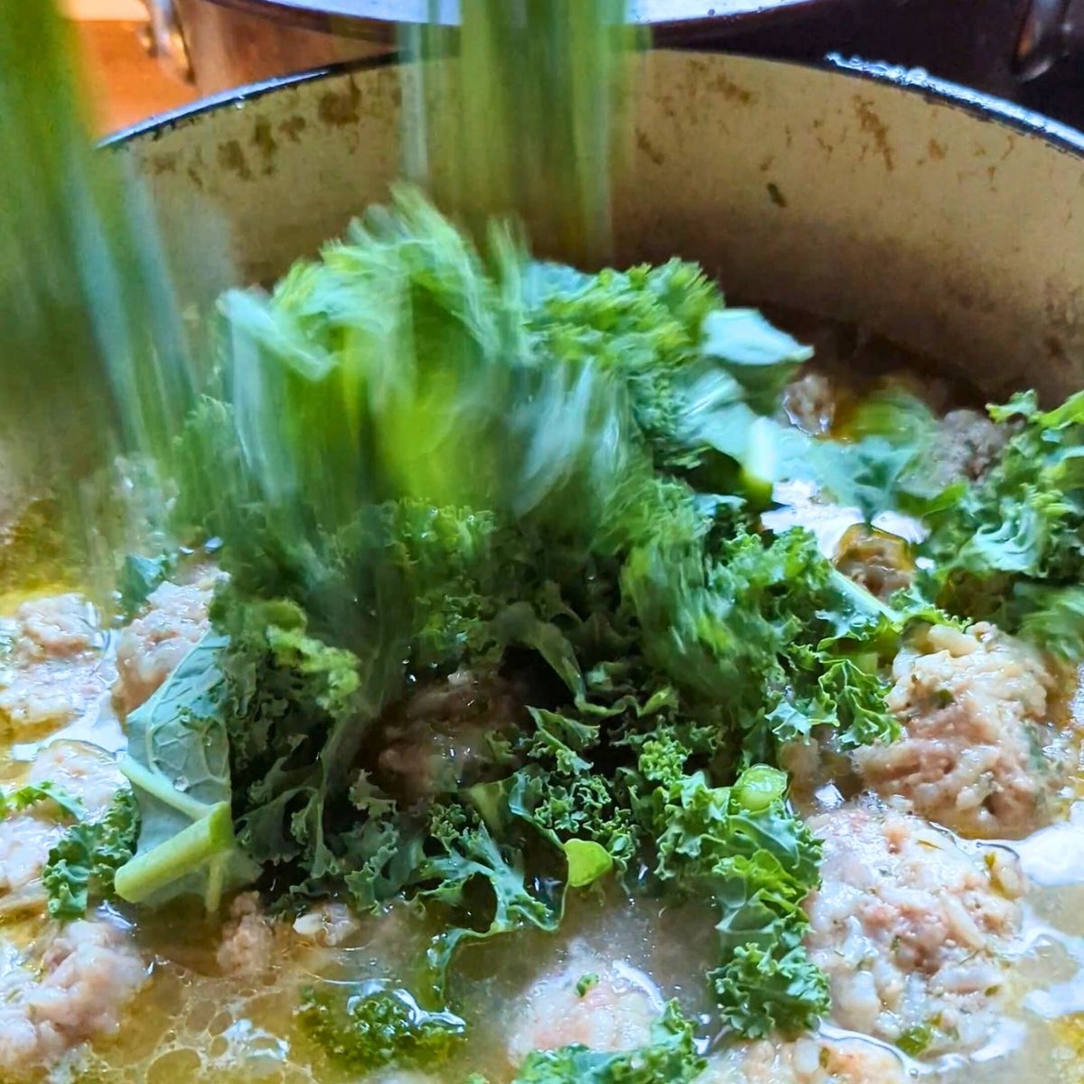 escarole added to youvarlakia soup with meatballs and fresh greens