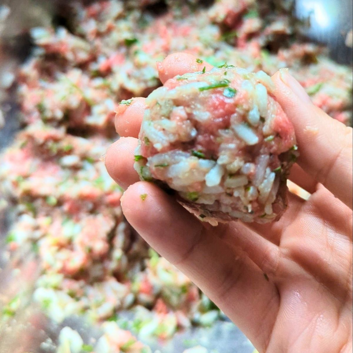 a hand forming youvarlakia meatballs with rice and parsley