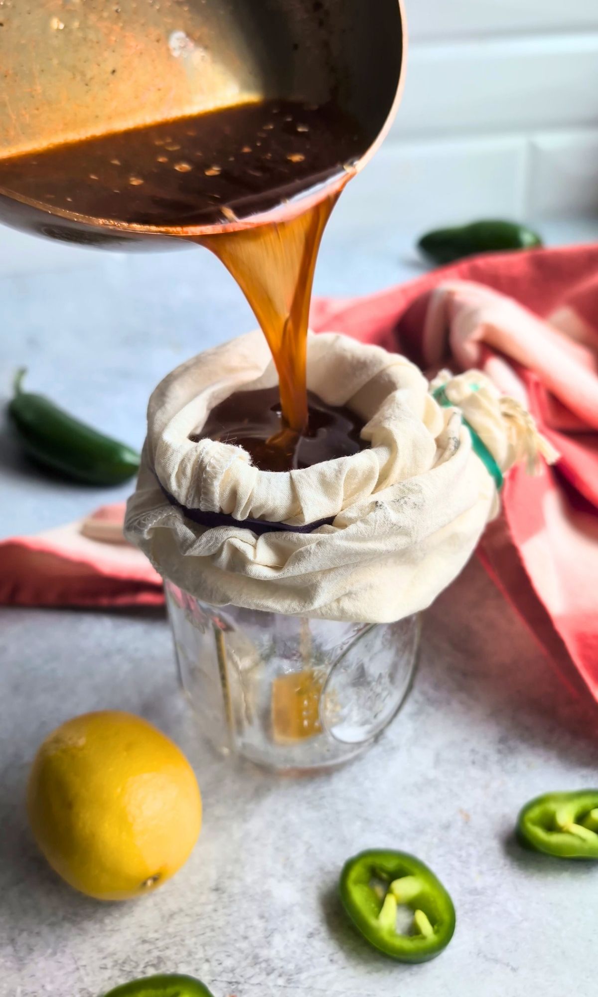 hot honey being strained through cheesecloth into a mason jar on the counter.