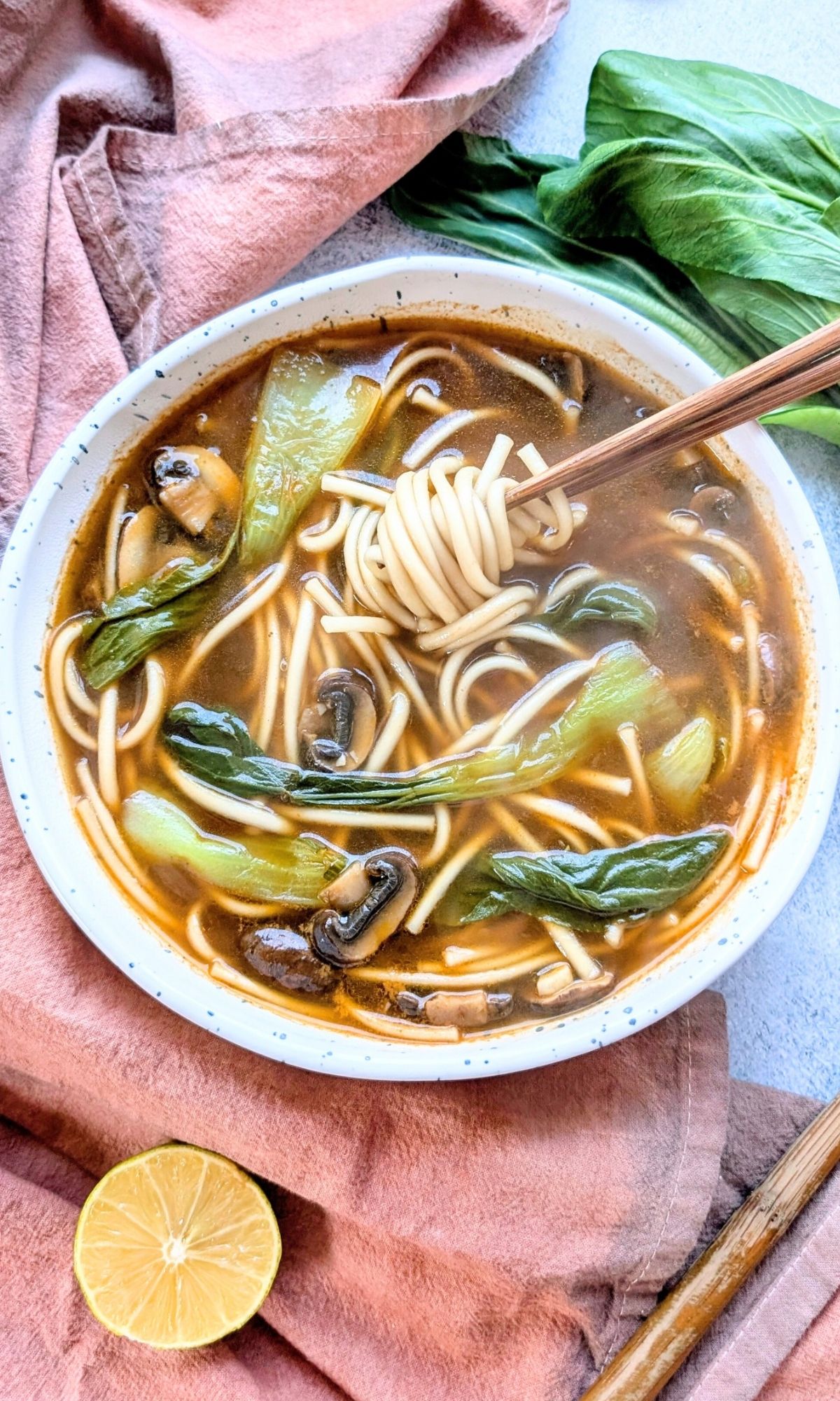 a bowl of udon soup with chopsticks on a japanese hand dyed napkin with greens and mushrooms for lunch.