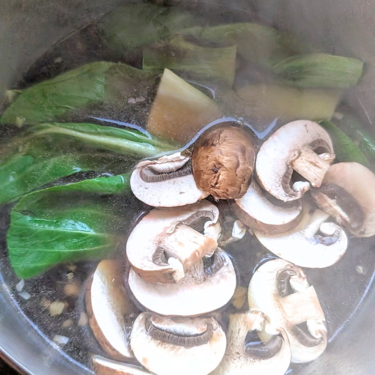 vegan udon soup with mushrooms and bok choy being cooked in a pot for a quick wfh lunch.