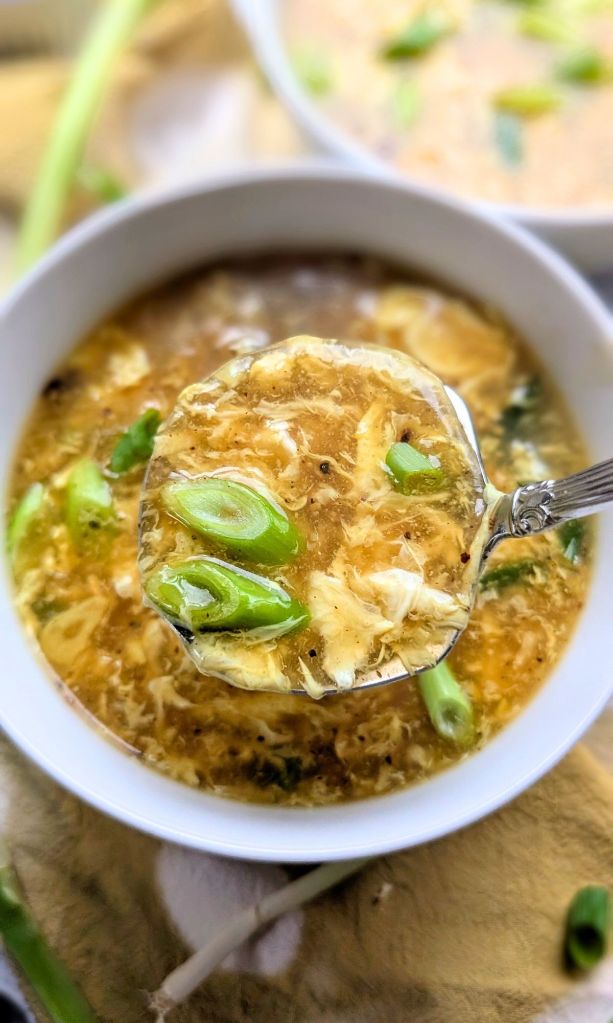 a ladle of egg drop soup in a bowl with fresh chopped scallions on top