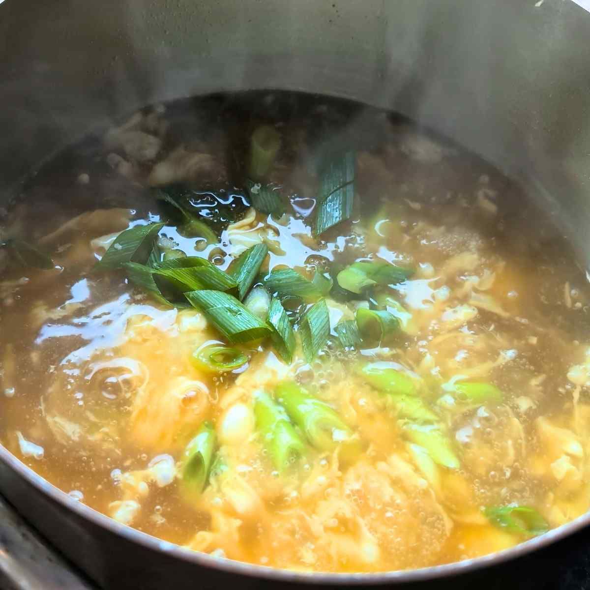 green onions or scallions being added to a pot of egg drop soup to garnish.