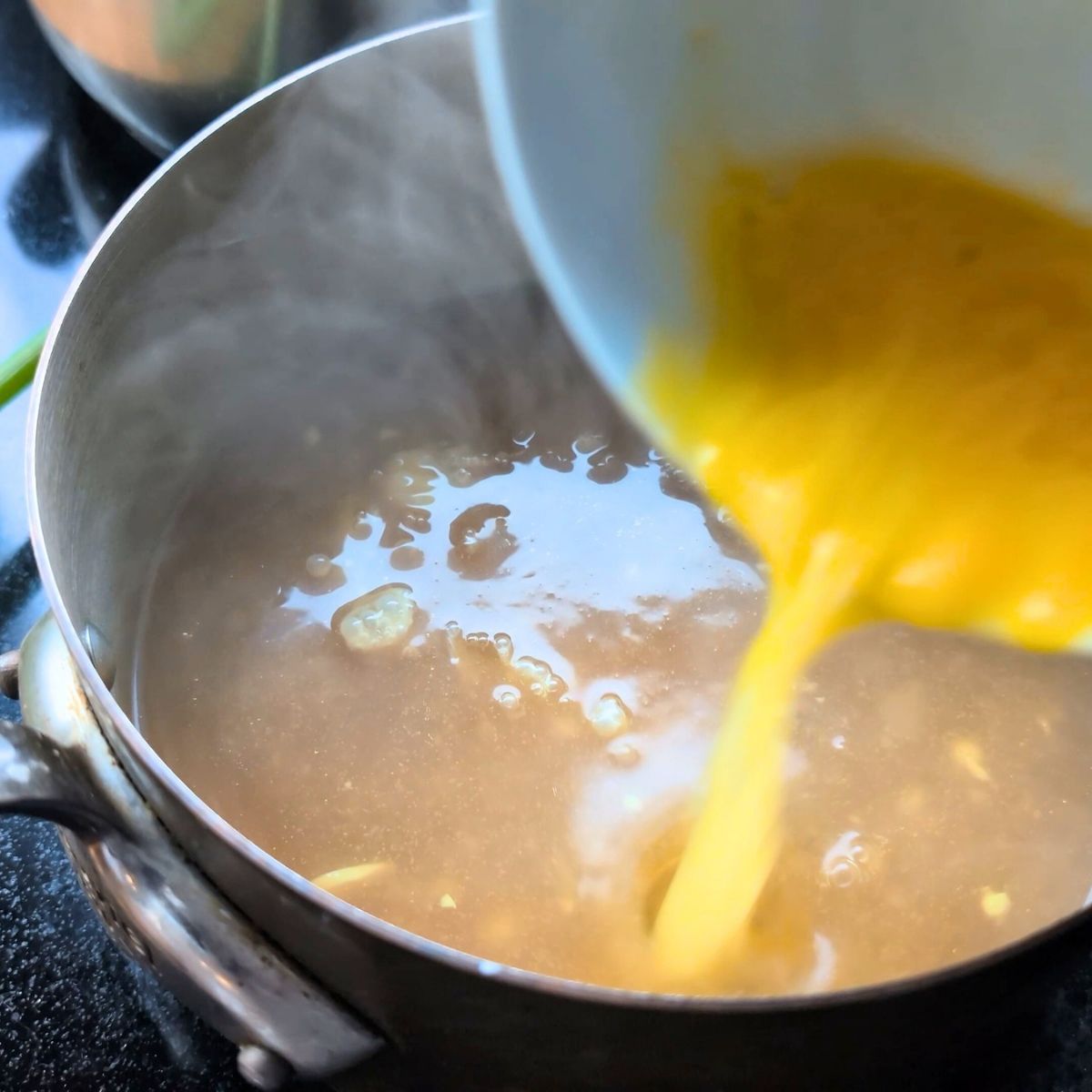 lightly beaten eggs being stirred into egg drop soup