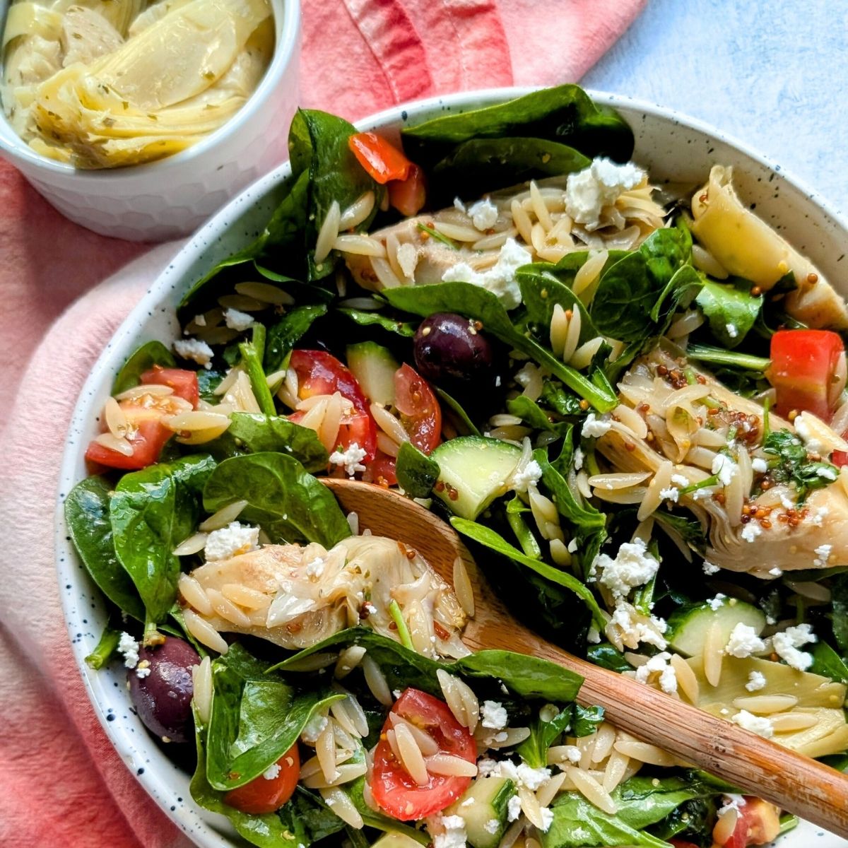 orzo salad with artichoke hearts and spinach and tomatoes.