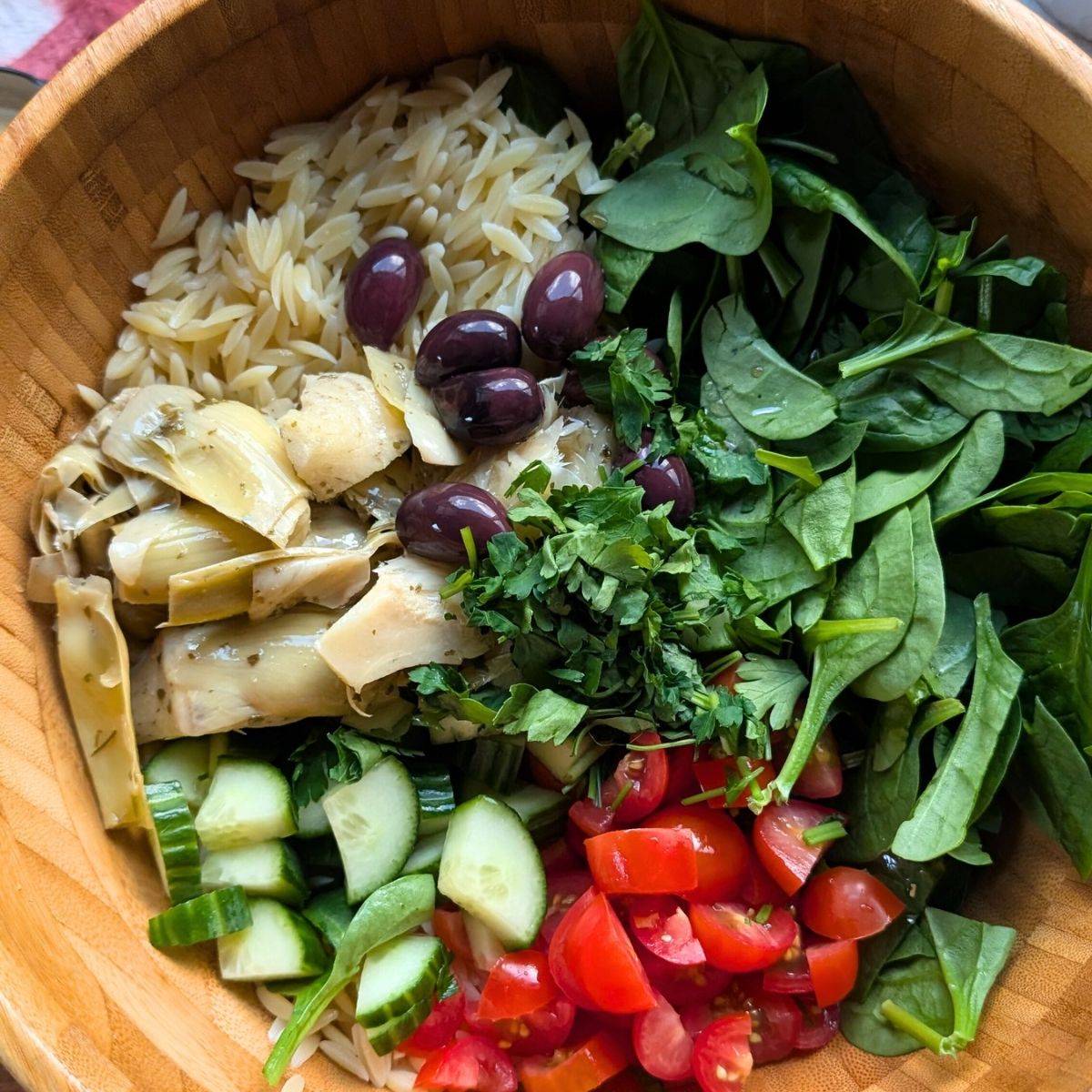 a large bowl of artichoke pasta salad with spinach, tomatoes, cucumber, and olives.