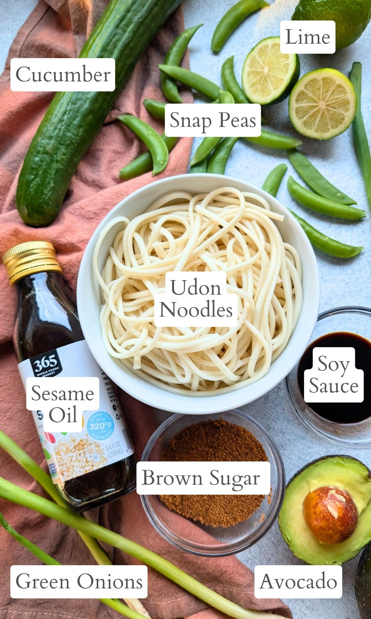 ingredients for udon noodle salad like sesame oil, limes, soy sauce, avocado, snap peas, and cucumber.