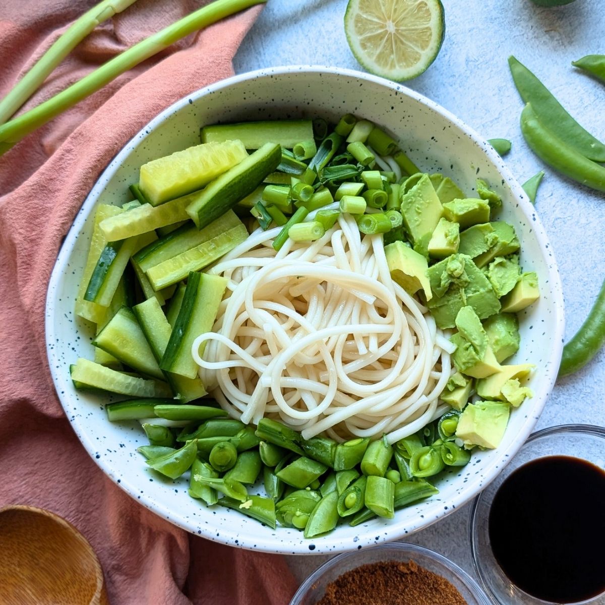 udon noodles in a bowl with cucumber avocado snap peas and green onions.