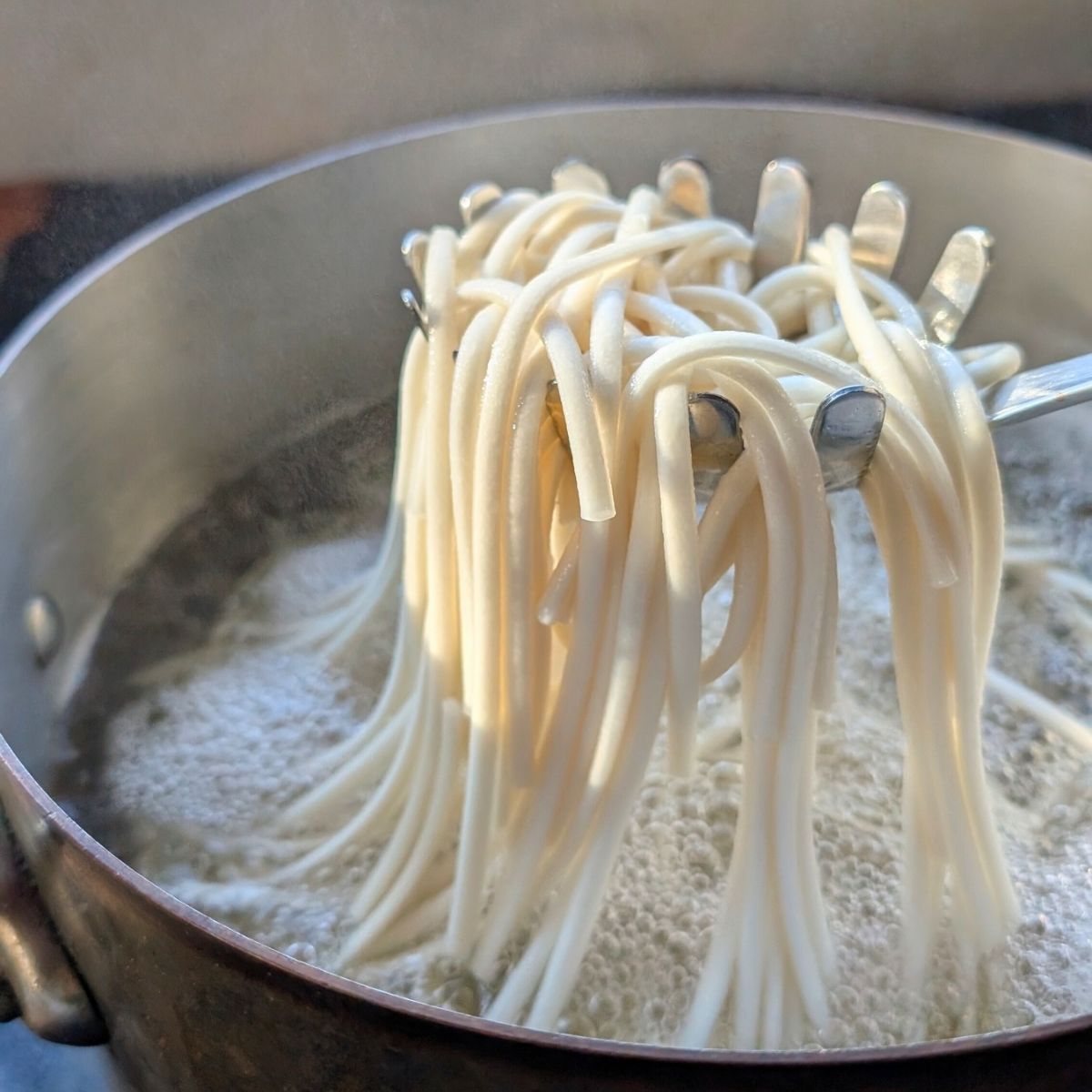 cooked udon noodles in a pot being strained to make peanut free udon noodle salad.