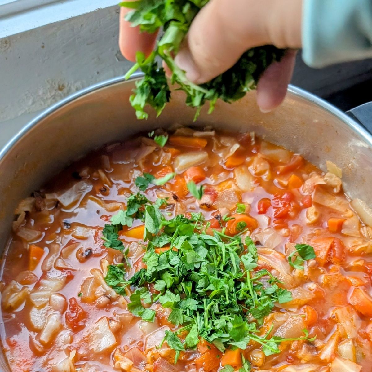 Chopped parsley being added to cabbage bean soup for a cozy winter vegan and vegetarian meal idea.