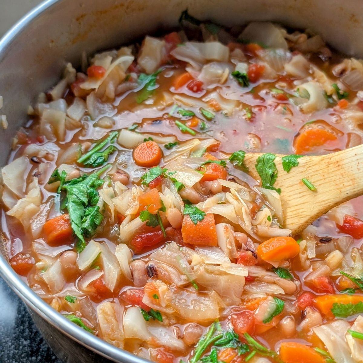 a large pot of cabbage and bean soup with fresh parsley, carrots, tomatoes, and vegetables.