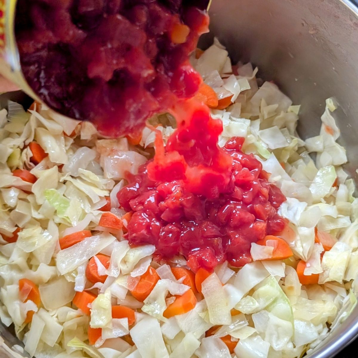 diced tomatoes added to a pot to make bean and cabbage soup