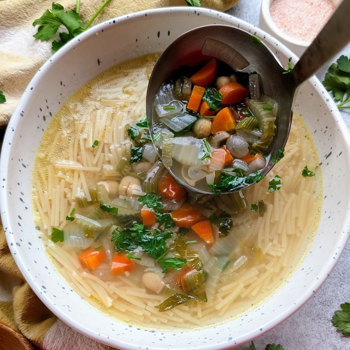 a ladle of hot soup pored over cooked noodles for parsley soup recipe