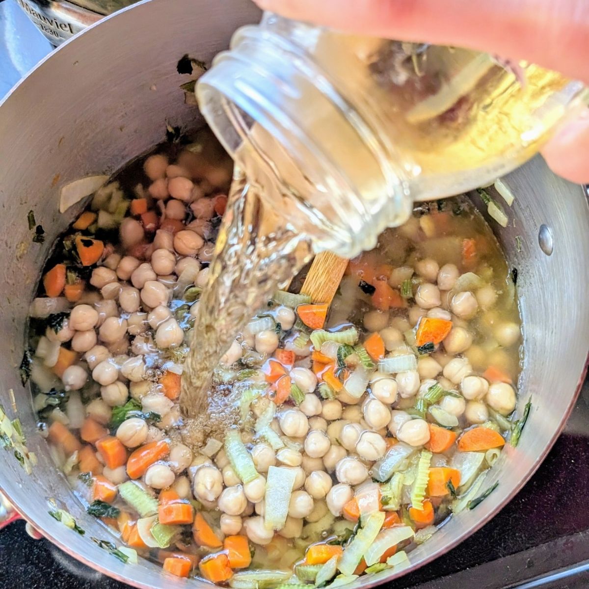 vegetable stock being added to chickpeas and fresh vegetables to make a soup