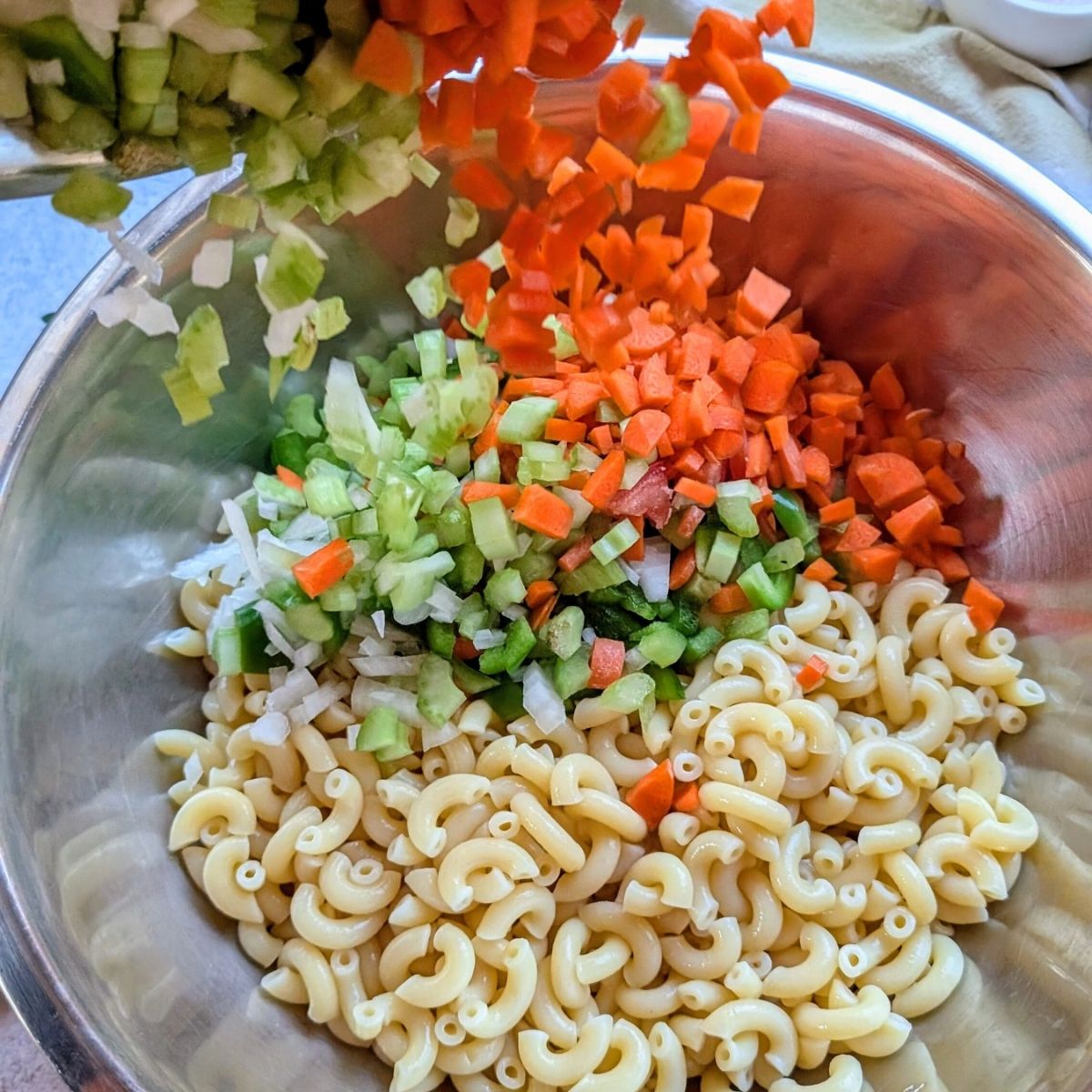 chopped celery, carrots, and onion added to a large bowl of cooled macaroni to make macaroni salad.