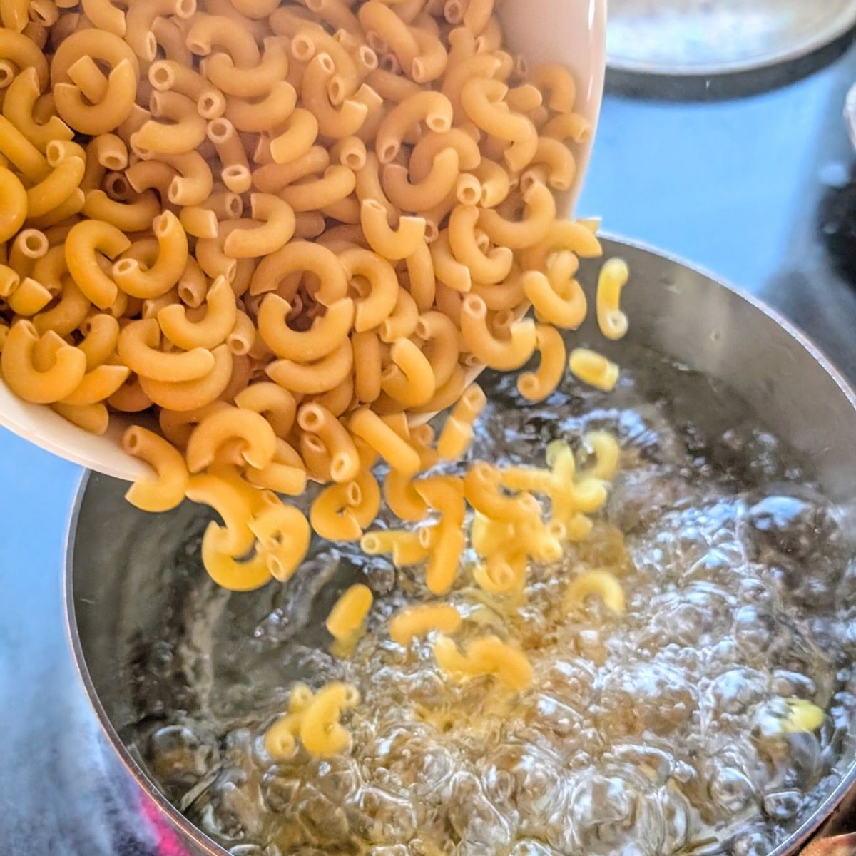 dried macaroni noodles being added to a boiling pot of water to make macaroni salad